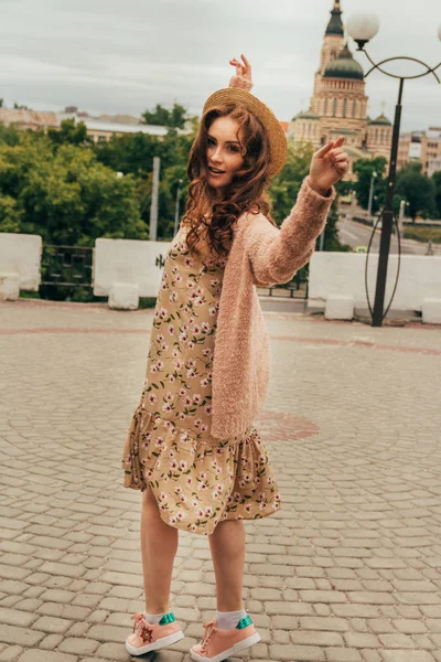 Mutlu kız elbise ve şapka bir şehir sokak ve kamera bakarak gülümsüyordu. bir şapka, bir çiçek ve sıcak renk bir ceket elbise