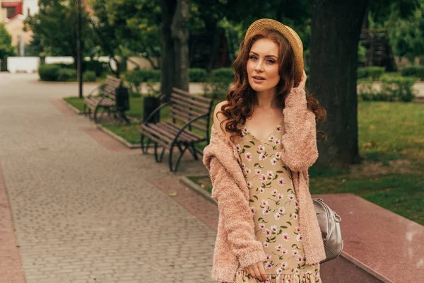 Mutlu kız elbise ve şapka bir şehir sokak ve kamera bakarak gülümsüyordu. bir şapka, bir çiçek ve sıcak renk bir ceket elbise