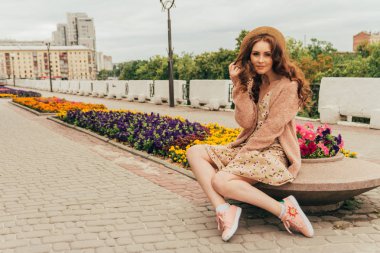 şapkalı, güzel bir kız saç rüzgardan tutar. şehir etrafında yürümek. Kızıl saçlı bir kız portresi. Çiçek, bej kazak ve hasır şapka bej elbise. aşk ve cinsellik. bir çiçek yatak çiçeklerle oturur. pozlar