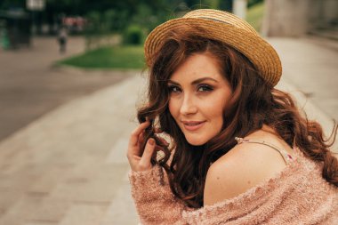 şapkalı, güzel bir kız saç rüzgardan tutar. artıkları üzerinde oturur. şehir etrafında yürümek. Kızıl saçlı bir kız portresi. Çiçek, bej kazak ve hasır şapka bej elbise. aşk ve cinsellik. flört