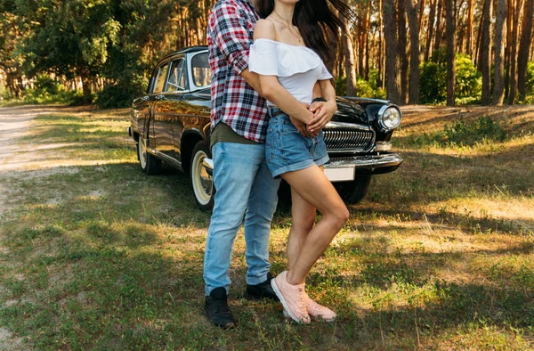 Love and affection between a young couple at the park. a guy in a plaid plane and jeans, a girl in shorts and a white jacket. They get together in the forest for a walk, near the old car. in the hands of wild flowers