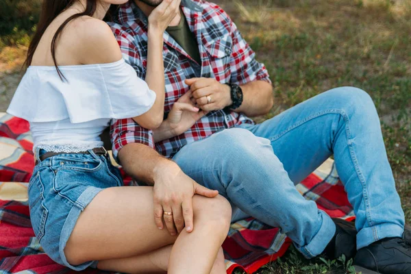 男と少女はプラッド ベール 草の上に座っています 格子縞のシャツとジーンズ 彼の腕に時計の男白ブラウスとデニムの Shorts Holding の手に身を包んだ少女 少女の Foot — ストック写真