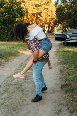 Kız adamın back.he üzerinde atladı legs.check üstünü tutar ve jeans.in arka plan siyah bir araba ormandaki