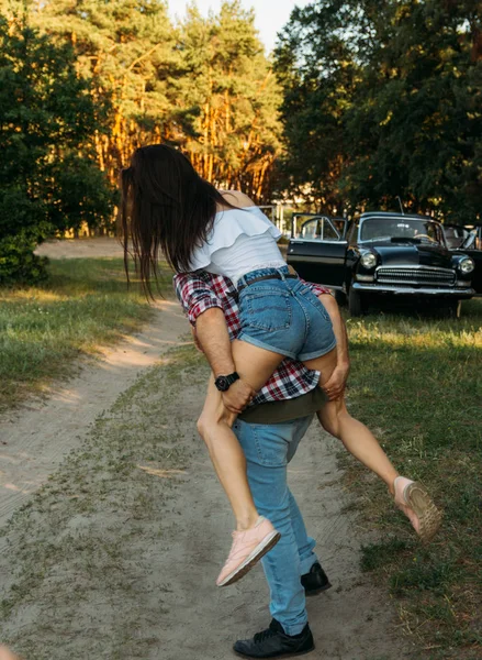 Back に飛びついた少女は 彼女の Legs Check シャツを保持し Jeans 背景は森の中の黒い車 — ストック写真