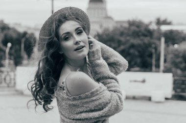 şapkalı, güzel bir kız saç rüzgardan tutar. artıkları üzerinde oturur. şehir etrafında yürümek. Kızıl saçlı bir kız portresi. Çiçek, bej kazak ve hasır şapka bej elbise. aşk ve cinsellik. flört. BSW. siyah beyaz fotoğraf