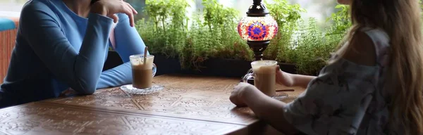 girlfriends enjoying in cafe together. Young women meeting in a cafe.meeting two women in a cafe for coffee. blue dress, dress in a flower, on a carved table is a cups of coffee and a lamp.