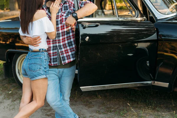 Arabayı kapıya yaslanmış bir adam siyah bir araba fonunda sarılma bir çift ayakta. bir adamın hand.horizontal fotoğraf siyah nöbette. bir adam bir kadının belinden hugs, bir kadın bir erkek göğsüne elini koydu