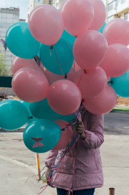 Kız, pembe bir ceket ve kot pantolon, bir sürü güzel pembe ve yeşil toplar, yüksek katlı ev ve gökyüzünün zemin karşı onlara, kelebekler ile dalga deniz rengini tutar.