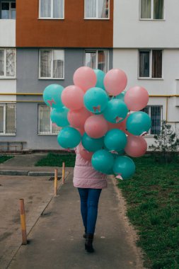 Kız, pembe bir ceket ve kot pantolon, bir sürü güzel pembe ve yeşil toplar, yüksek katlı ev ve gökyüzünün zemin karşı onlara, kelebekler ile dalga deniz rengini tutar.