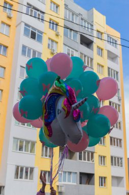 mavi, yeşil ve pembe pembe kelebekler ile renkli topları bir grup, bir şişme çok renkli tek boynuzlu at, binanın arka planı tutan eller