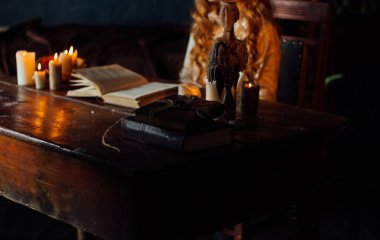 eski vintage ahşap bir şamdan mumlar ile geçerli. Kızıl saçlı bir kız vintage giysiler içinde mum ışığında ahşap bir masa üzerine bir kitap eski kitap okuma masada oturuyor