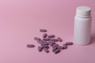 bir beyaz hap şişesi üzerinde pembe bir arka plan. depolama hapları. vitaminler. hapları bırakın. ve mor haplar, haplar yalan birbirine yakın.