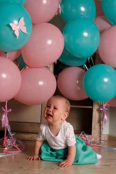 a little girl, a child, sits on the floor and cries, wrinkled her nose, near the balloons, a holiday. birthday, turned a year old. dress is white and blue. resentment, disappointment.the child cries, gets angry.frustrated baby. cry