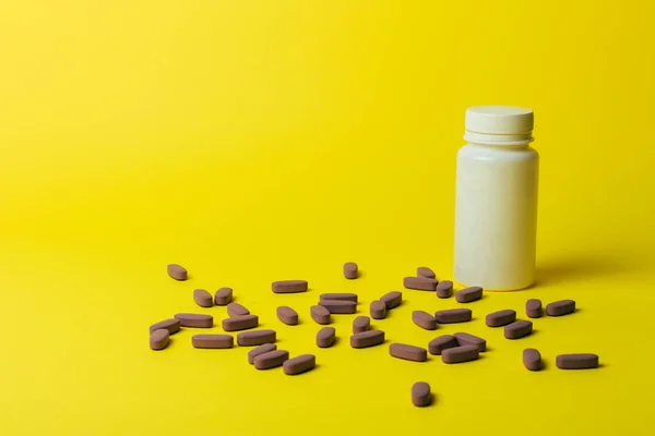 one white pill bottle on yellow background. storage pills. vitamins. release pills. and purple pills, pills lie next to each other.