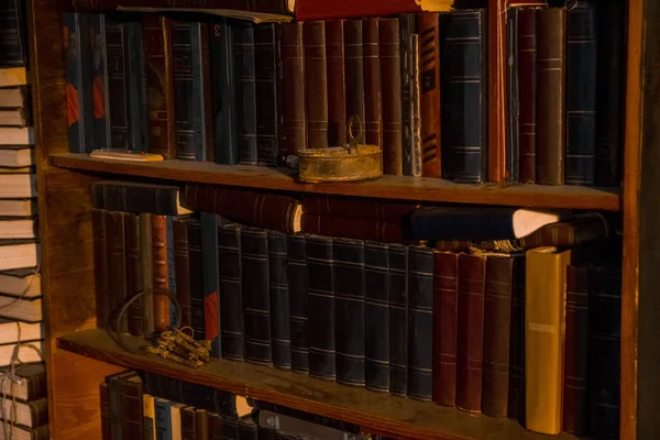 old books stand on wooden shelves, shelving with books. on the shelf is an old, rusty lock and a bunch of keys, the concept of science, the door to education, training