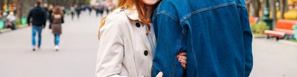 girl in a beige coat holding the hand of a guy in a denim jacket who is trying to leave, parting, leaving, breaking up.In the background a lot of people in the blur, the concept of personal drama, loneliness among the crowd