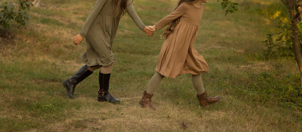 two girls, teenagers, holding hands, walk on green grass, side view.in a brown and green dress, autumn walk, early autumn. village days. best friends. friendship between girls.run in nature