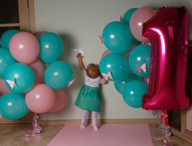 küçük çocuk ulaşan ilk Doğum günü balonları, yakındaki bir ışık düğmesi için. merak. beyaz mavi elbiseli kız