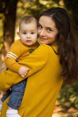 Mutlu genç anne ile bebek ile sarı Akçaağaç Sonbahar parkta oynarken bırakır. Aile açık havada yürüyüş sonbaharda. Sonbaharda parkta oynarken annesi ile küçük çocuk.