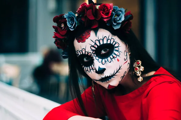 a girl with a painted face of a skeleton, a dead zombie, in the city during the day. day of all souls, day of the dead, halloween, ghost walk Santa Muerte