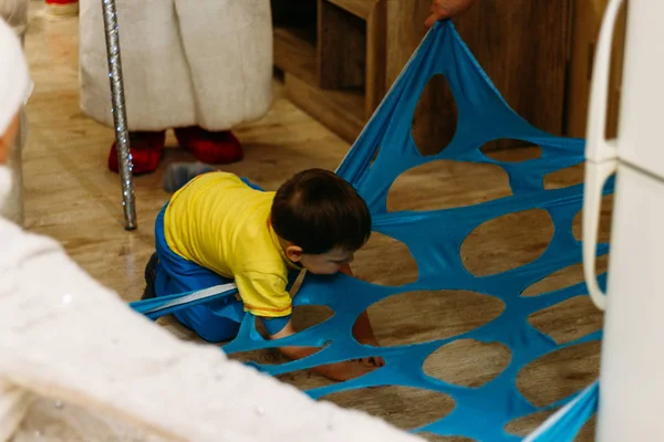 a small boy steps over, climbs, rails, passes into a hole, a cut, an opening in a blue fabric, in matter. child Game. tunnel, labyrinth. child playing the game