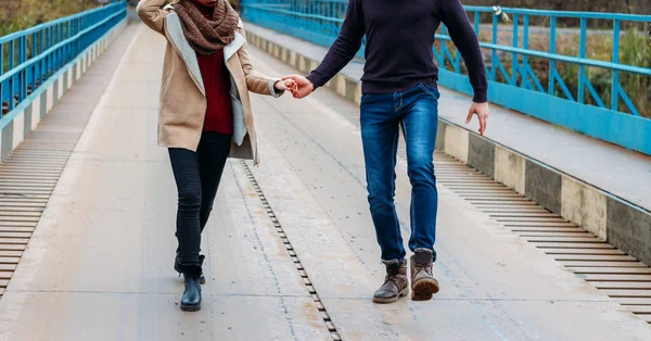Пара біжить і стрибає по мосту, тримаючись за руки, біля води, осінь. любов і сім'я, побачення в парку біля річки — стокове фото