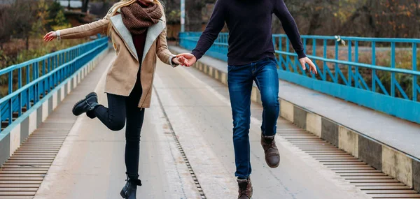 Пара пробежек и прыжков на мосту, держась за руки, у воды, осень. любовь и семья, свидание в парке у реки — стоковое фото