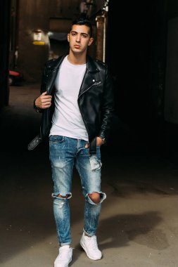 Genç, yakışıklı bir beyaz gömlek, siyah, deri ceket ve mavi, yırtık kot biri sokak, modeli, şehirde yürümek, canlı Style.in'ın beyaz spor ayakkabı