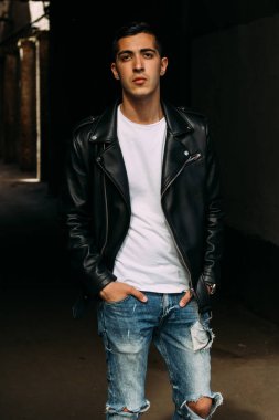 Genç, yakışıklı bir beyaz gömlek, siyah, deri ceket ve mavi, yırtık kot biri sokak, modeli, şehirde yürümek, canlı Style.in'ın beyaz spor ayakkabı