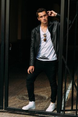 Genç, yakışıklı beyaz tişört, siyah, deri ceket ve siyah pantolon sokak, n T-shirt güneş gözlüğü biri. modeli, şehirde yürümek, canlı Style.in'ın beyaz spor ayakkabı