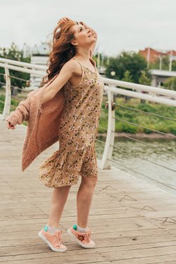 Romantik kız elbise ve sıcak renkler bir kazak giyiyor şehirde, saçları rüzgarda geliştirir. gülümseyen ve başım dönüyor. şapkasını devam ediyor