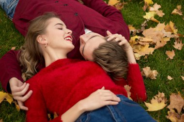 Çift bir kız ve bir adam kırmızı kazak, başkanları, dudak yakın, sevgi ve cazibe bir Close-up çim üzerinde yalan gülümseyerek. kiss.love ikinci bir tarih. Çift sarı yapraklarda yatıyor