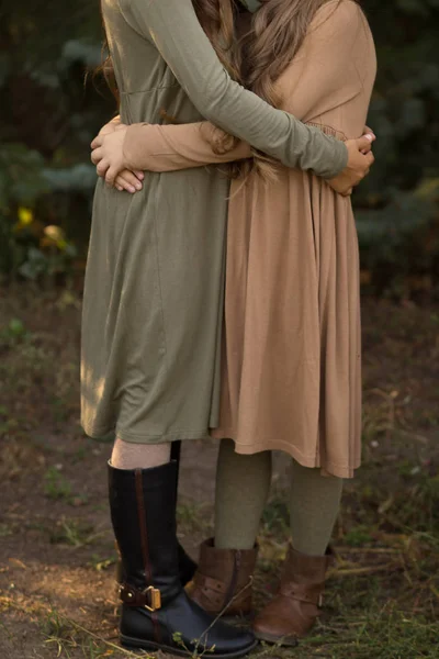 two girls hug on the street in the forest. friendship. in green and brown dress. a park. autum