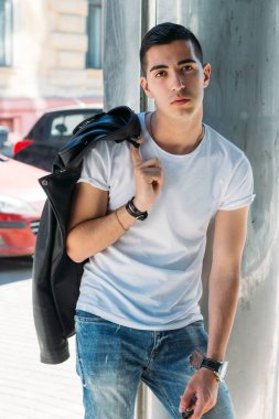 Genç, yakışıklı bir beyaz gömlek, siyah, deri ceket ve mavi, yırtık kot biri sokak, modeli, şehirde yürümek, canlı Style.in'ın beyaz spor ayakkabı. bir saat el, parlak güneş parlar, yaz