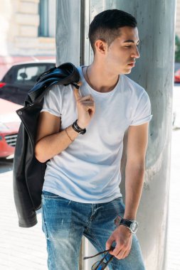 Genç, yakışıklı bir beyaz gömlek, siyah, deri ceket ve mavi, yırtık kot biri sokak, modeli, şehirde yürümek, canlı Style.in'ın beyaz spor ayakkabı. bir saat el, parlak güneş parlar, yaz