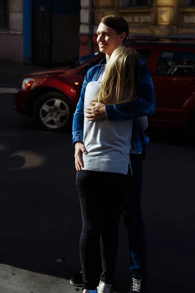 A dark background.A loving and happy couple is hugging on the street, amid a red car, the guy smiles and holds his hand on the girl\'s waist. summer spring