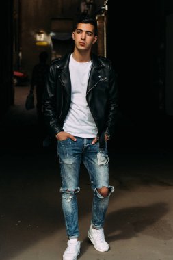 Genç, yakışıklı bir beyaz gömlek, siyah, deri ceket ve mavi, yırtık kot biri sokak, modeli, şehirde yürümek, canlı Style.in'ın beyaz spor ayakkabı