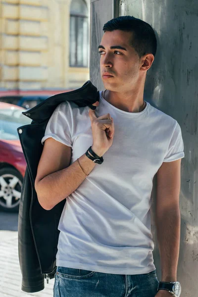 Genç, yakışıklı bir beyaz gömlek, siyah, deri ceket ve mavi, yırtık kot biri sokak, modeli, şehirde yürümek, canlı Style.in'ın beyaz spor ayakkabı. bir saat el, parlak güneş parlar, yaz