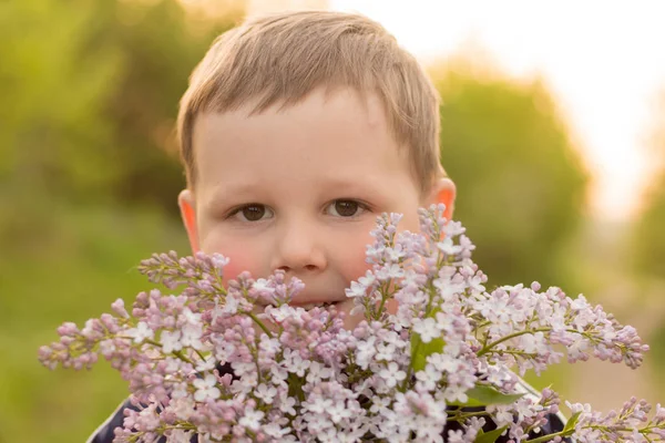 Портрет мальчика с сиренью. букет фиолетовой сирени в руках у детей. руки держат фиолетовый букет сиреневых цветов на лугу . — стоковое фото