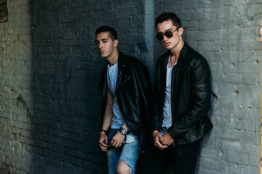 güzel ve çekici adam şehirde ayakta, poz. siyah deri kurta, beyaz T-shirt, kot pantolon ve beyaz ayakkabı giymiş. ayna Binası yakınında. siyah gözlük şehirde dolaşmak. iletişim. Toplantı arkadaşlar.