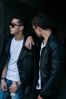 güzel ve çekici adam şehirde ayakta, poz. siyah deri kurta, beyaz T-shirt, kot pantolon ve beyaz ayakkabı giymiş. ayna Binası yakınında. siyah gözlük şehirde dolaşmak. iletişim. Toplantı arkadaşlar.