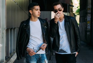 güzel ve çekici adam şehirde ayakta, poz. siyah deri kurta, beyaz T-shirt, kot pantolon ve beyaz ayakkabı giymiş. ayna Binası yakınında. siyah gözlük şehirde dolaşmak. iletişim. Toplantı arkadaşlar.