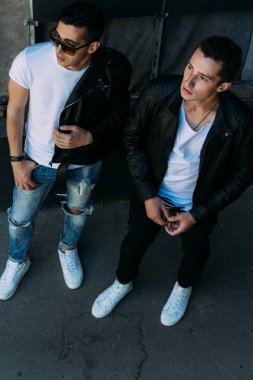 güzel ve çekici adam şehirde ayakta, poz. siyah deri kurta, beyaz T-shirt, kot pantolon ve beyaz ayakkabı giymiş. ayna Binası yakınında. siyah gözlük şehirde dolaşmak. iletişim. Toplantı arkadaşlar.