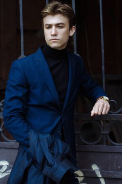 kameraya bakarak bir takım elbise ve siyah kazak, yakın çekim, eline altın bir saat, düşünceli poz, çekici bir adam portresi.