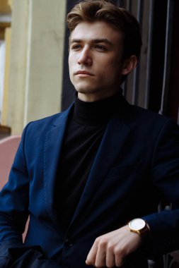 kameraya bakarak bir takım elbise ve siyah kazak, yakın çekim, eline altın bir saat, düşünceli poz, çekici bir adam portresi.