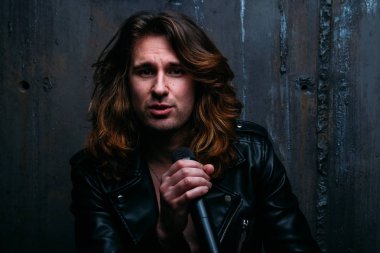 bir acımasız, yakışıklı adam, karanlık bir arka plan bir sandalyeye oturur ve onun hands.presenter, concert.sings, şarkıcı bir mikrofon tutar bir şarkıcı portresi