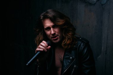 bir acımasız, yakışıklı adam, karanlık bir arka plan bir sandalyeye oturur ve onun hands.presenter, concert.sings, şarkıcı bir mikrofon tutar bir şarkıcı portresi