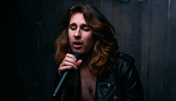 portrait of a brutal, handsome man, a singer who sits on a chair on a dark background, and holds a microphone in his hands.presenter, singer at the concert.sings