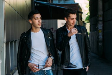 güzel ve çekici adam şehirde ayakta, poz. bir siyah deri ceket, beyaz T-shirt, kot pantolon ve beyaz ayakkabı giymiş. ayna Binası yakınında. siyah gözlük şehirde dolaşmak. iletişim. Toplantı arkadaşlar.