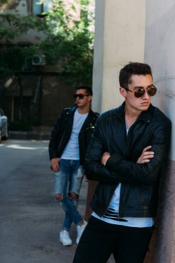 güzel ve çekici adam şehirde ayakta, poz. bir siyah deri ceket, beyaz T-shirt, kot pantolon ve beyaz ayakkabı giymiş. ayna Binası yakınında. siyah gözlük şehirde dolaşmak. iletişim. Toplantı arkadaşlar.